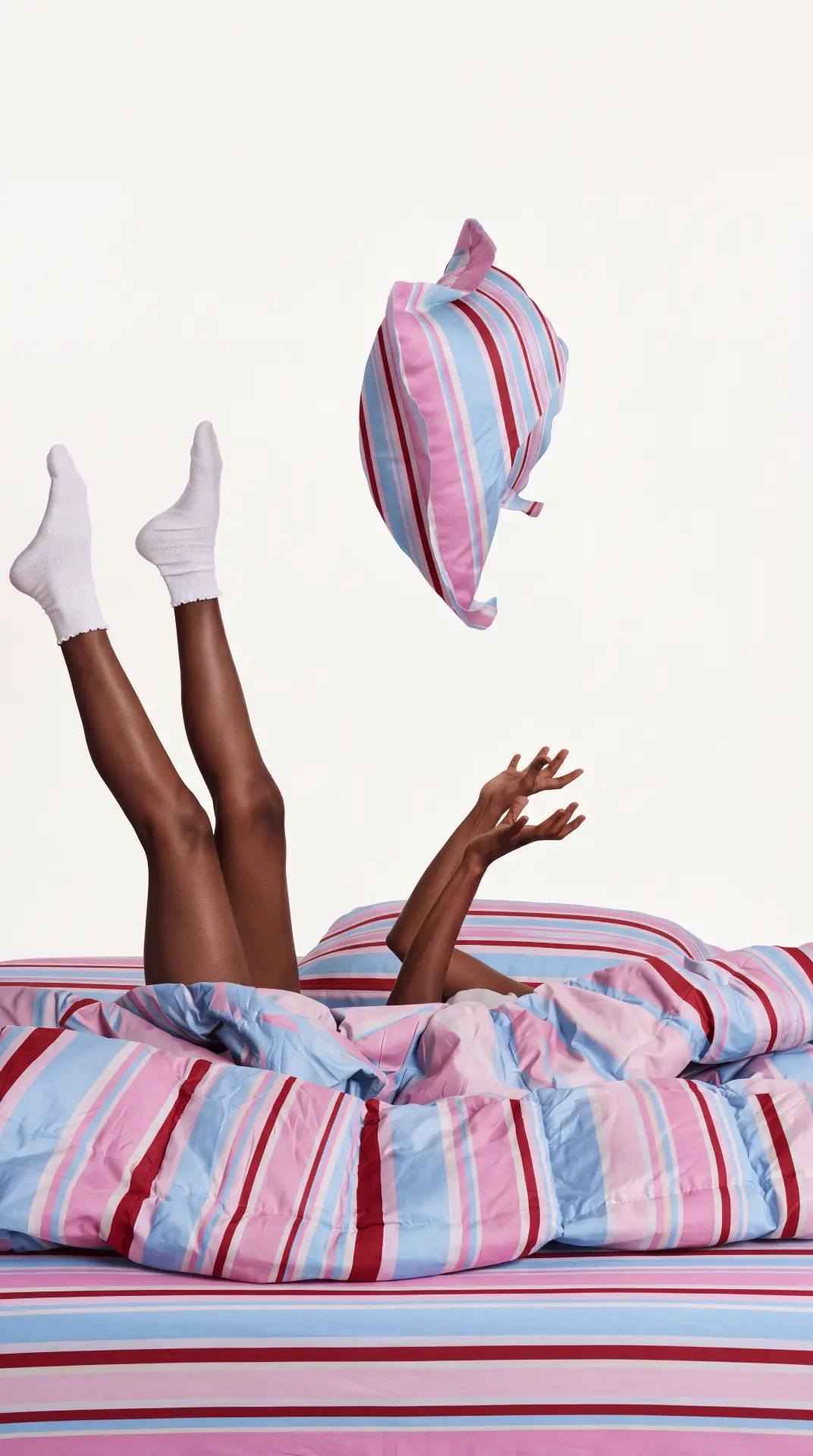A playful pillow toss above pink and blue striped bedding